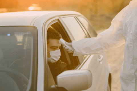 Image of masked man in car getting temperature taken